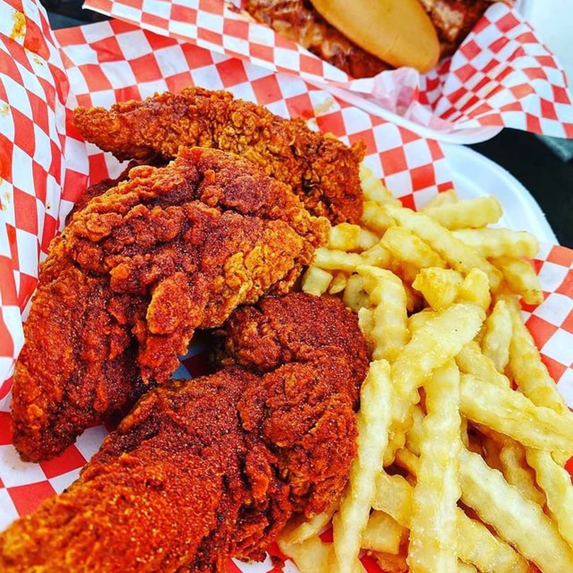 Spicy fried chicken tenders and crinkle-cut fries in a red and white checkered basket.