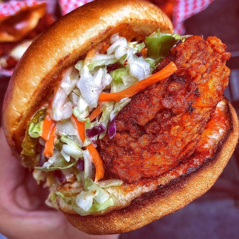 Close-up of a fried chicken sandwich from 2 Neighbor's, with coleslaw and pickles on a brioche bun.