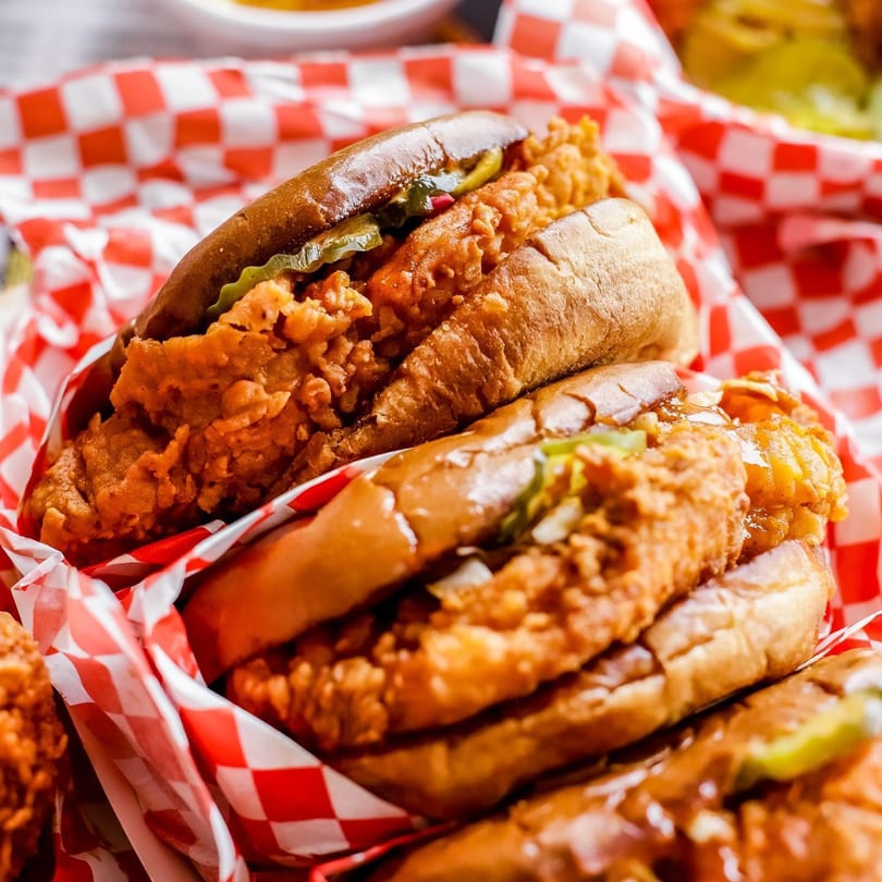 Two fried chicken sandwiches with pickles and sauce in red and white checkered paper.