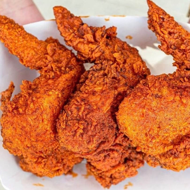 Close-up of several pieces of crispy, orange-red fried chicken from 2 Neighbor's in a white container.